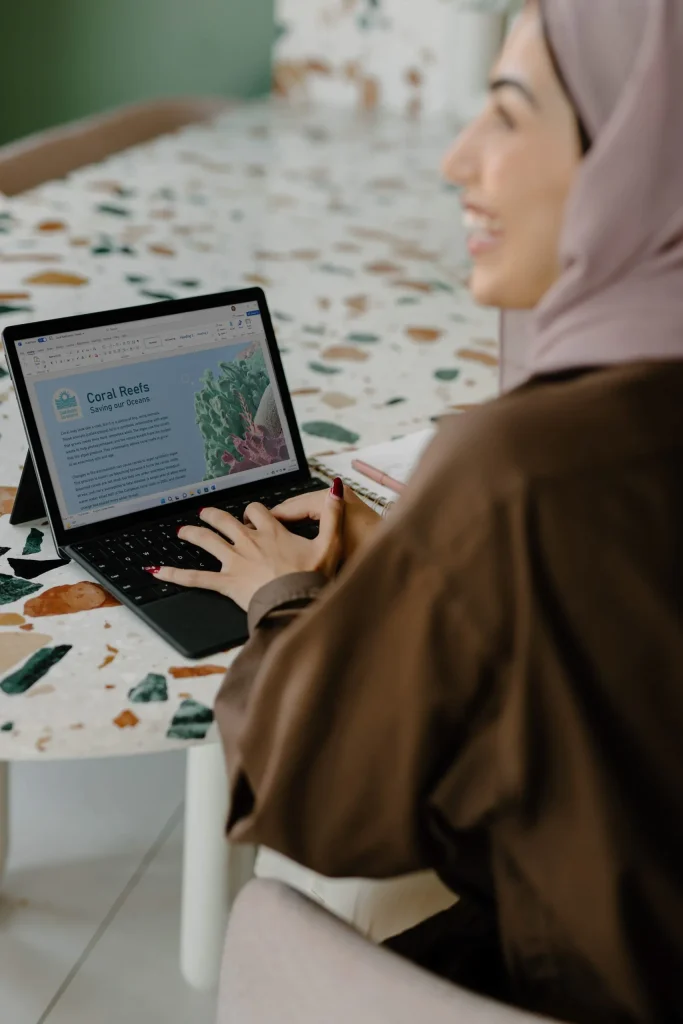 Une femme en hijab assise à une table avec un ordinateur portable.