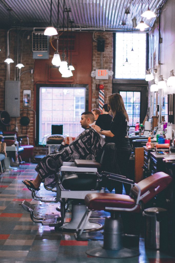 A man is getting a haircut in a barber shop, discussing social media marketing services for small businesses.