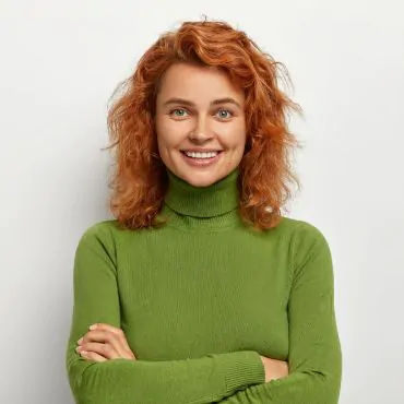 A smiling red haired woman in a green turtleneck sweater.