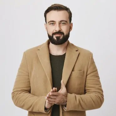 A bearded man in a tan coat posing for a photo.