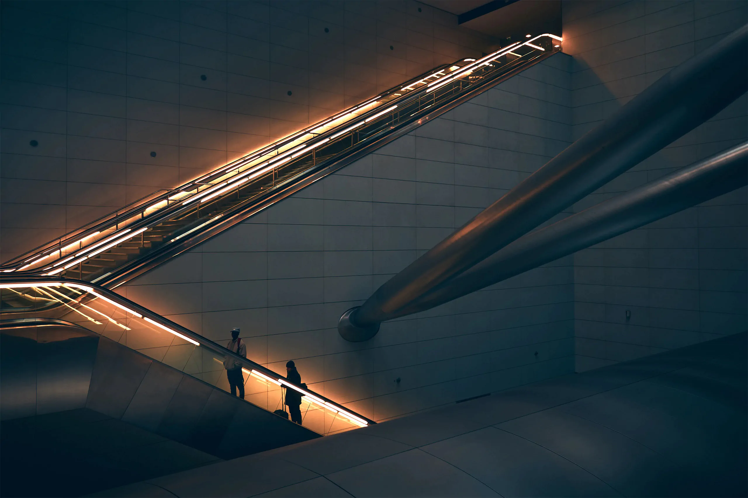 Personne debout sur un escalator dans un bâtiment moderne avec des accents d'éclairage chauds, représentatifs de l'esthétique d'une agence d'identité de marque.
