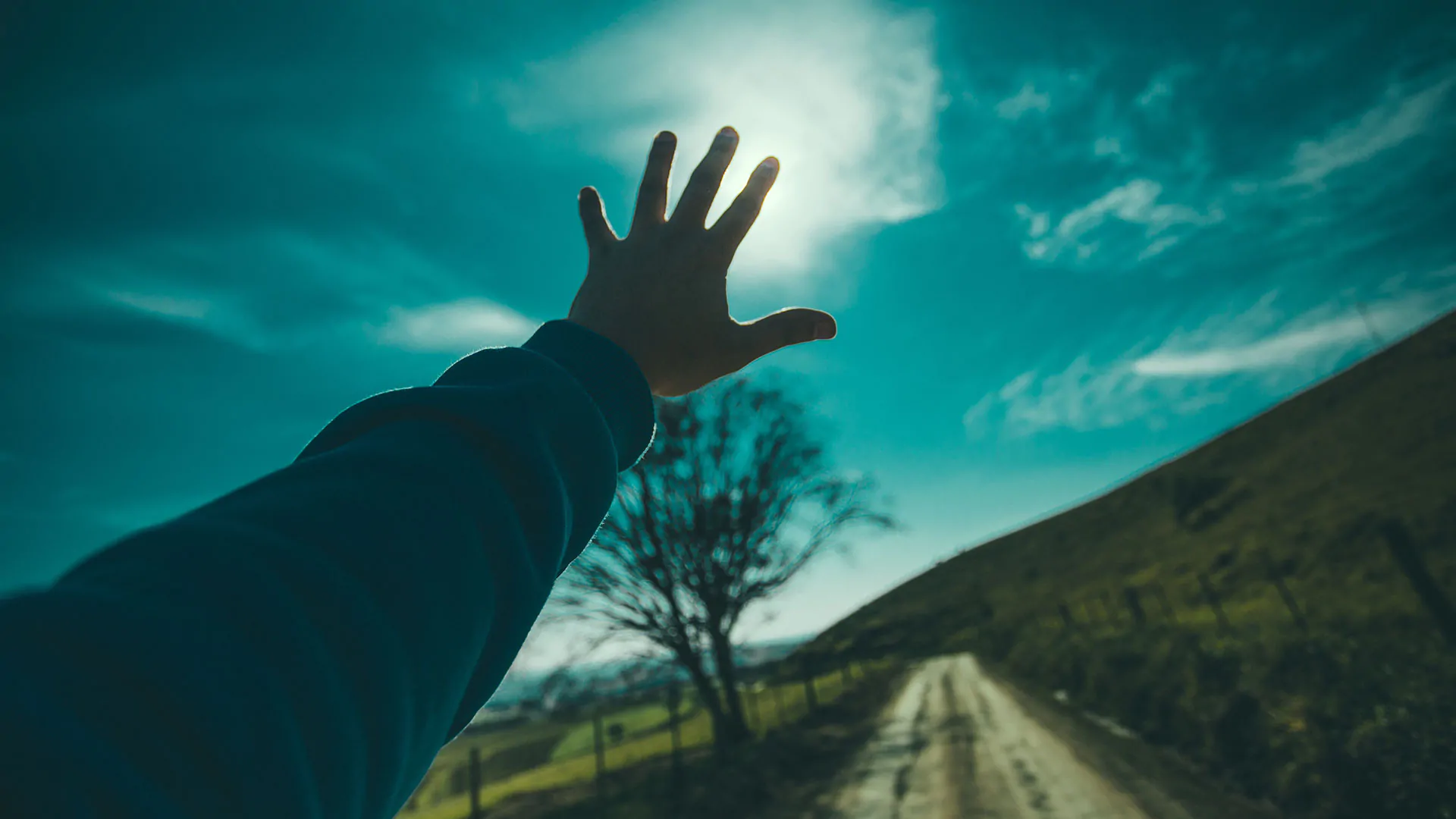 A person's hand reaching up to the sky on a dirt road, signaling the pioneering spirit of a marketing agency.